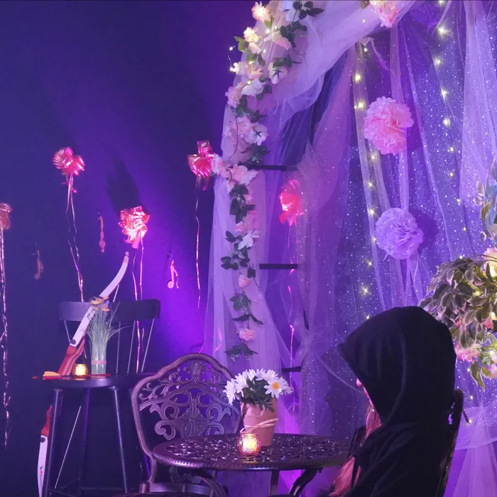 Un coin salon décoré de voilage, de guirlandes lumineuses et de fleurs, baigné d’une lumière violette.