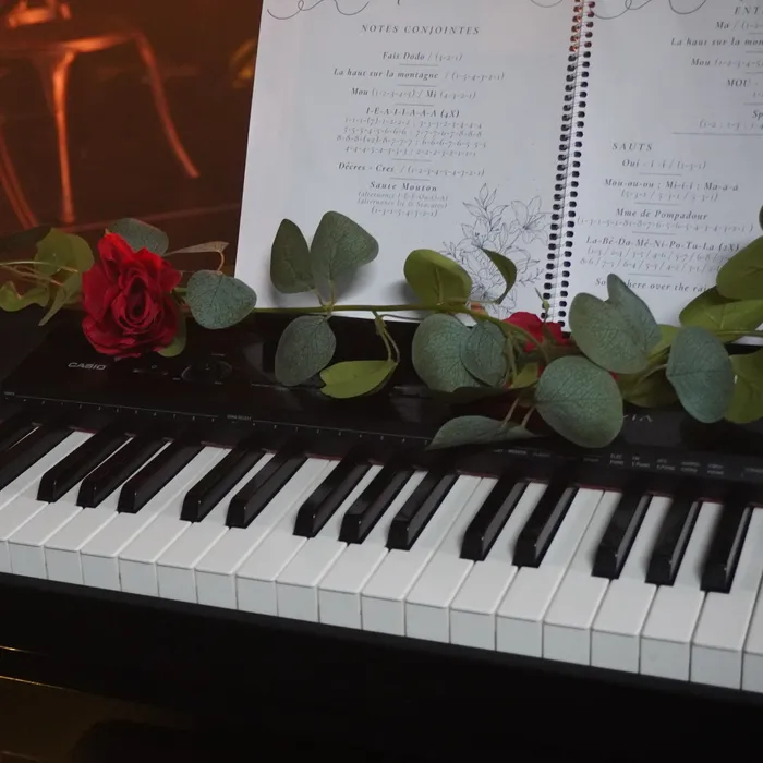 Un clavier orné d’une rose rouge et de feuillage, un cahier d’exercices vocaux ouvert sur le lutrin.
